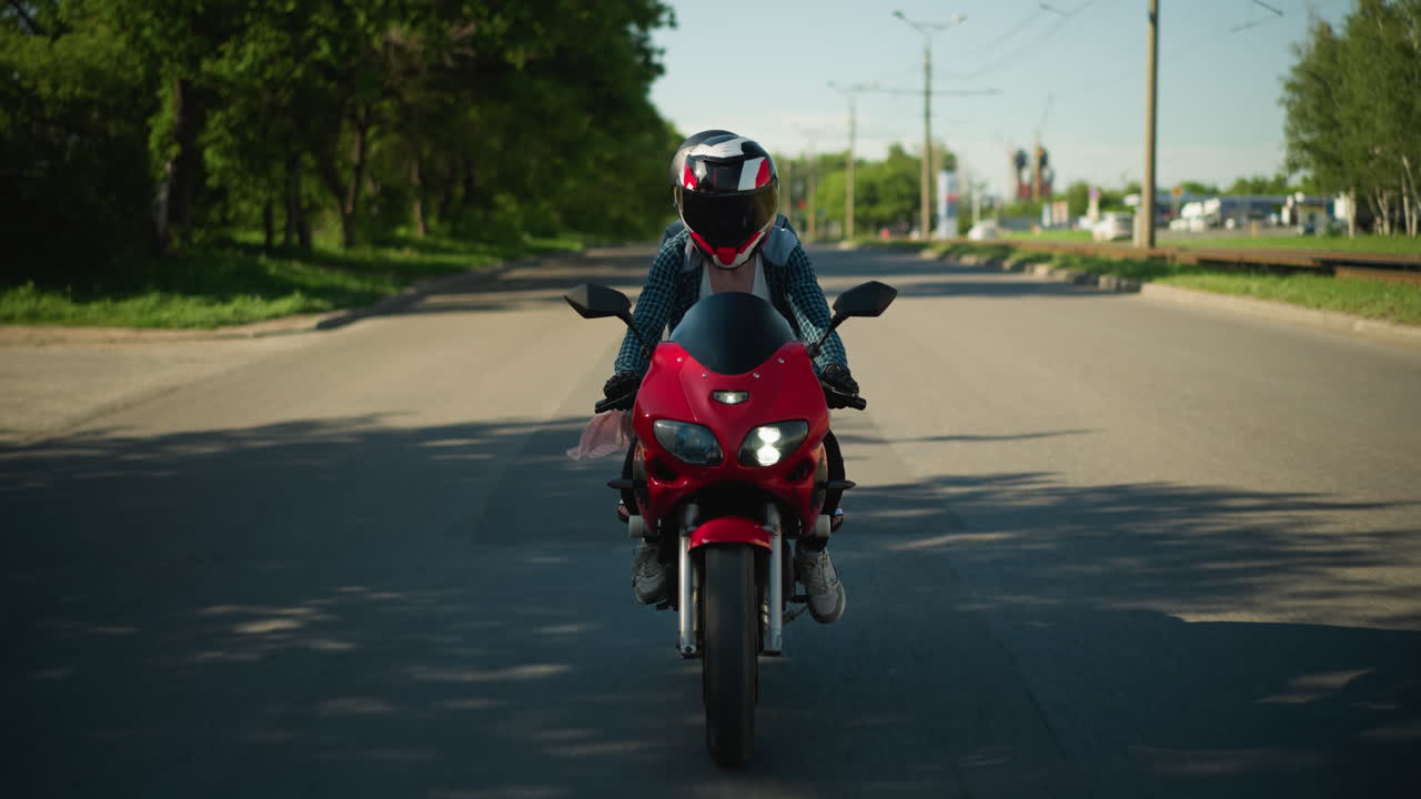 dos amigos montan una bicicleta eléctrica, ambos con cascos, a lo largo de una carretera asfaltada sombreada, las sombras de los árboles se proyectan a través de la carretera, mientras que se ven coches moviéndose en el carril opuesto
