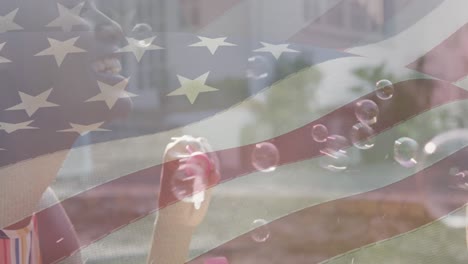 animación de la bandera de ee.uu. ondeando sobre madre e hijo afroamericanos haciendo burbujas de jabón