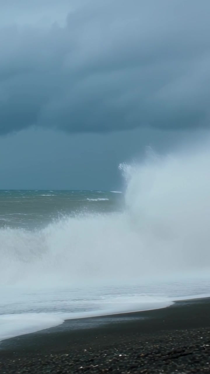 Vertical video: Driving storm waves hitting reef, spraying foam across black pebble shore