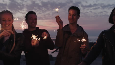 Retrato-De-Un-Grupo-De-Jóvenes-Amigos-Celebrando-La-Víspera-De-Año-Nuevo-Sosteniendo-Bengalas-Sonriendo-Feliz-Alegre-Disfrutando-De-Una-Fiesta-En-La-Playa