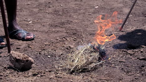 primer plano de un maasai encendiendo un fuego con hierba seca, técnicas tradicionales de hacer fuego
