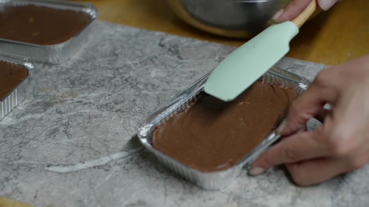 Crema al cioccolato spalmata su brownie in contenitore di alluminio usando un cucchiaio da cucina, filmato in primo piano in stile rallentato