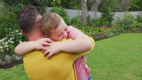 feliz padre caucásico con su hijo abrazando y llevando en el jardín