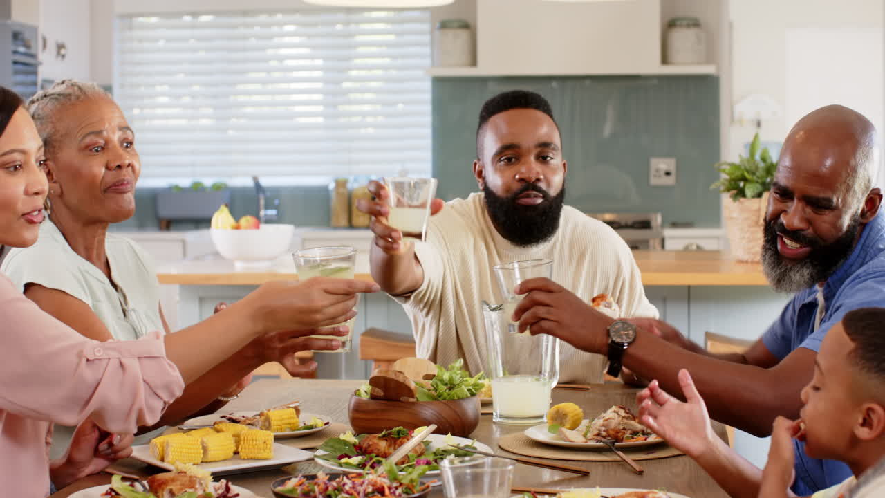 Family toasting with glasses, enjoying meal together at home dining table
