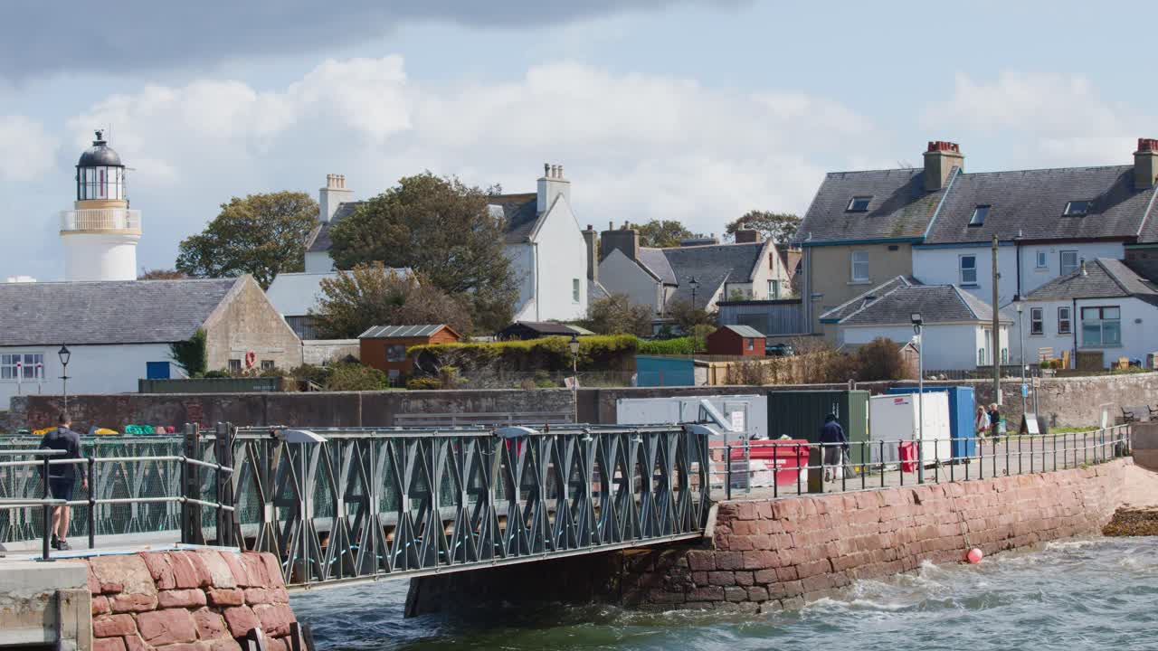 Daytime wide shot of Cromarty harbor bridge, lighthouse, historic buildings, and choppy coastal waters