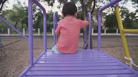 slow motion dolly in and out clip of an east asian boy kid having fun playing with colorful playground equipment outdoors