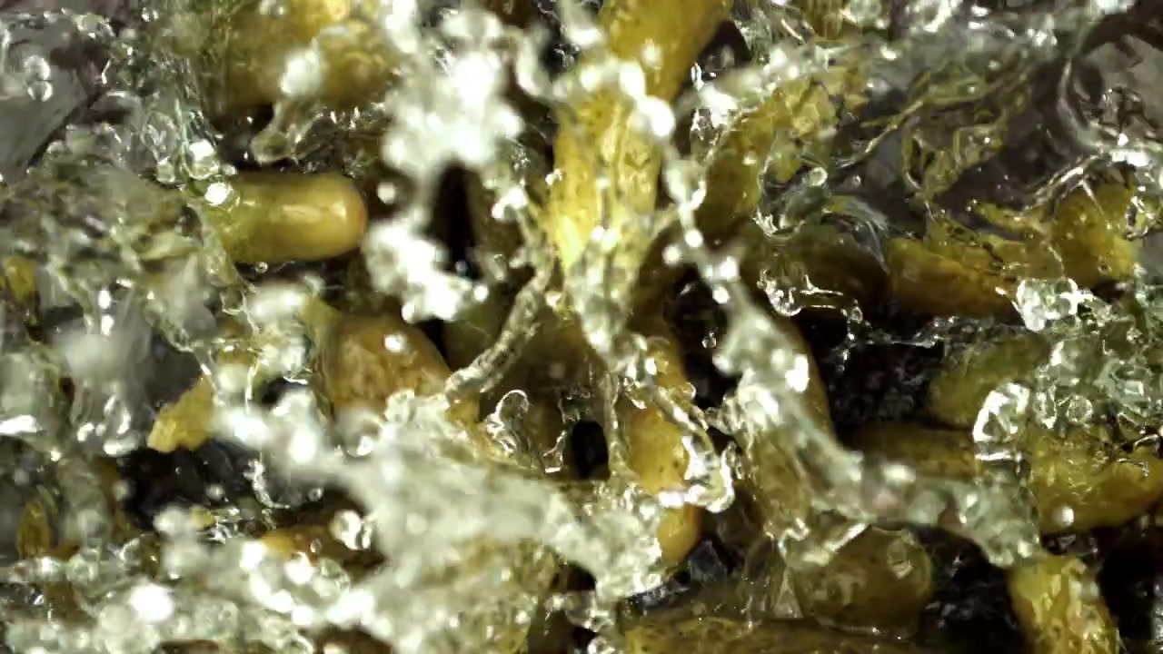 Små syltede agurker falder og plasker ned i vand i slowmotion