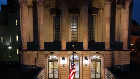 Rising-drone-shot-showing-american-flag-in-front-of-historic-church-at-night