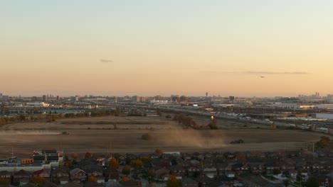 Traktor-Pflügt-Landwirtschaftliches-Ackerland,-Stadtbild,-Skyline-Gebäude,-Stark-Befahrene-Autobahn-Bei-Sonnenuntergang,-Ontario,-Kanada