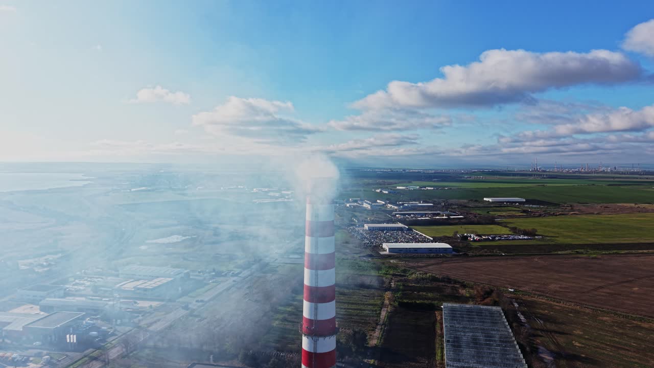 Industry and smoke rising from a tall chimney in open landscape