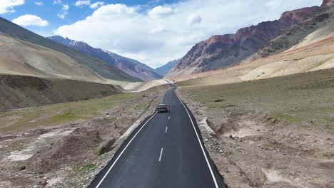 aerial drone shot displaying a car steadily moving on a straight, scenic road carved through the mountains.