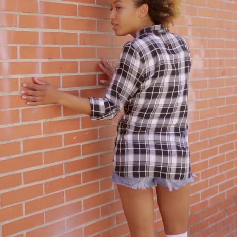 Rear-View-Of-Walking-Woman-Along-A-Brick-Wall