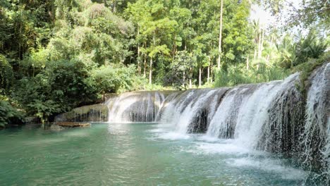 Tripod-shot-of-water-flowing-from-Cambugahay-Falls-into-natural-turquoise-pool-with-bamboo-raft-in-Siquijor-Island,-the-Philippines-in-ultra-slow-motion