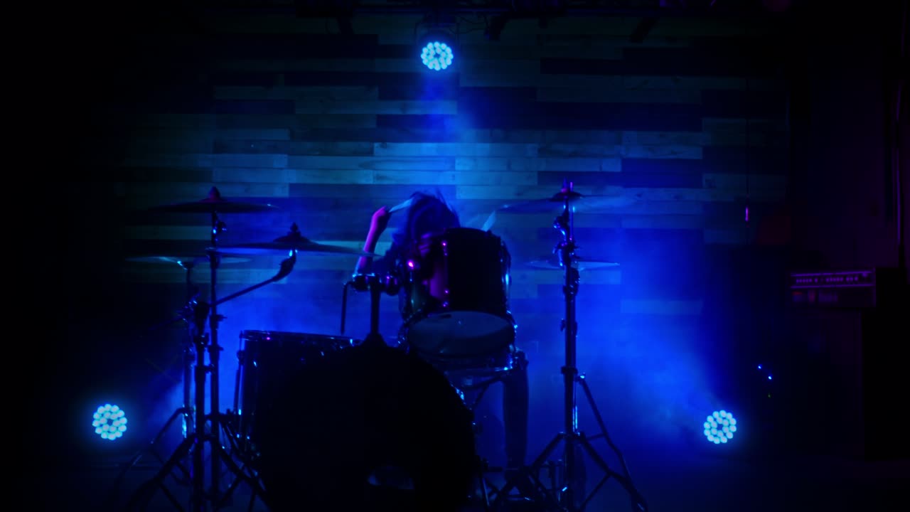 드러머 소녀는 파란색, 빨간색, 초록색의 불빛으로 활기차게 드럼을 연주합니다.