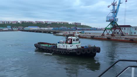 a tugboat navigates in a port with a crane in the background