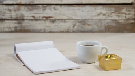 notepad, cup of black coffee and golden gift box on wooden surface 4k