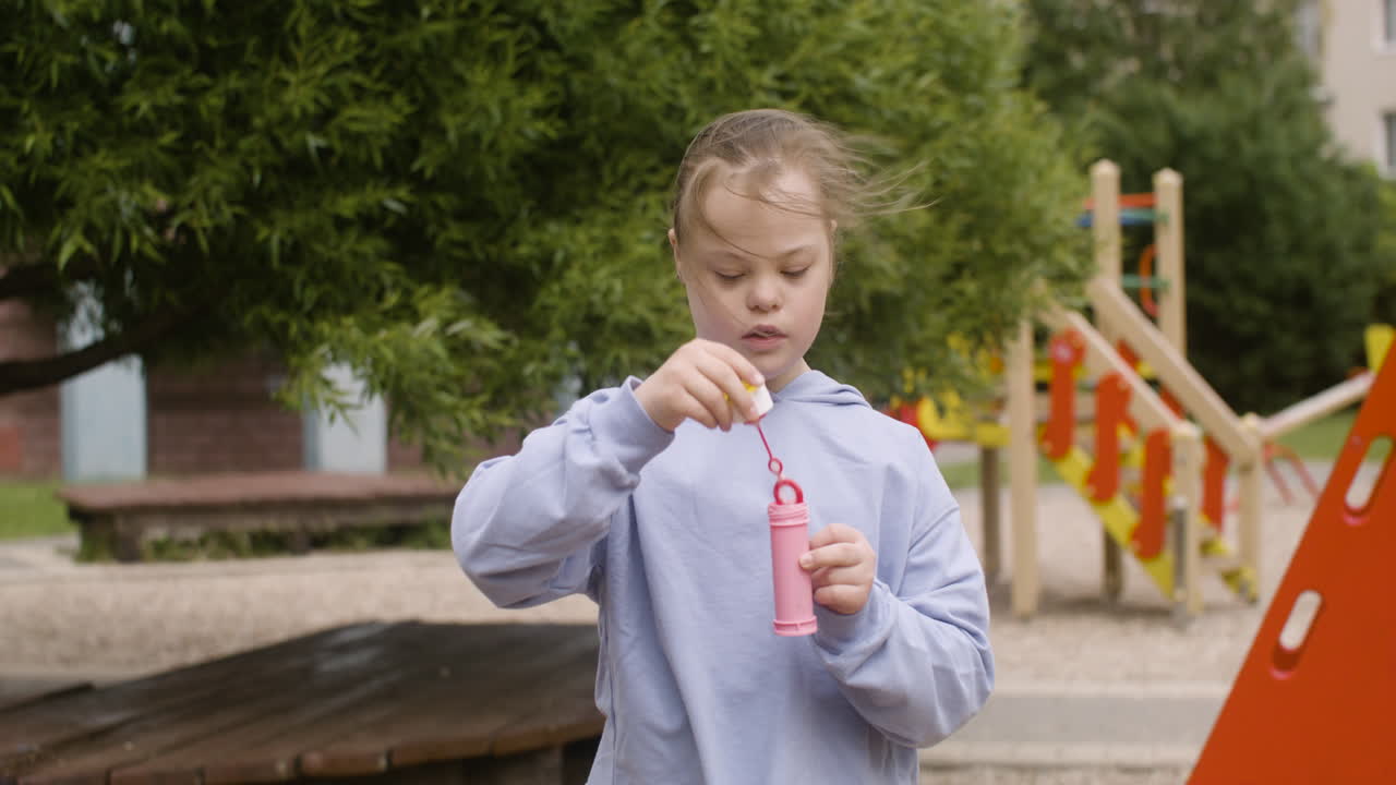 Little girl with down syndrome blowing soap bubbles in the park on a windy day