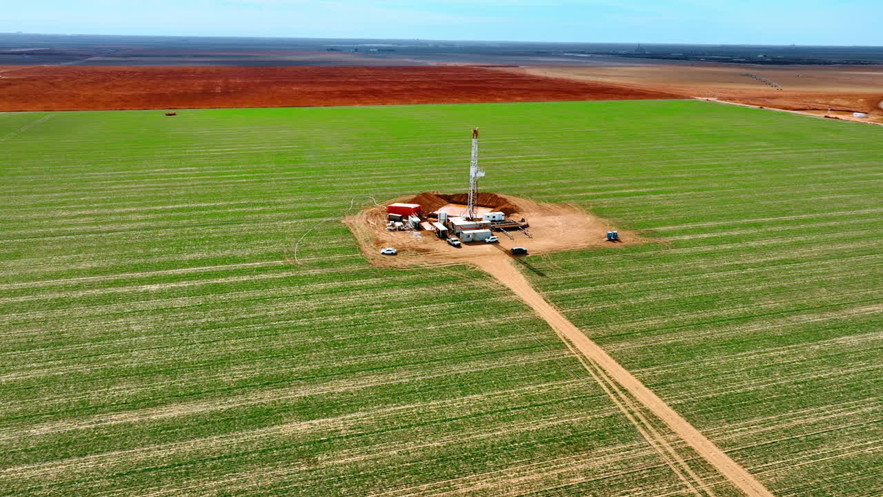 Green field with an oil rig in the middle. Little site for production of natural resources from aerial perspective.