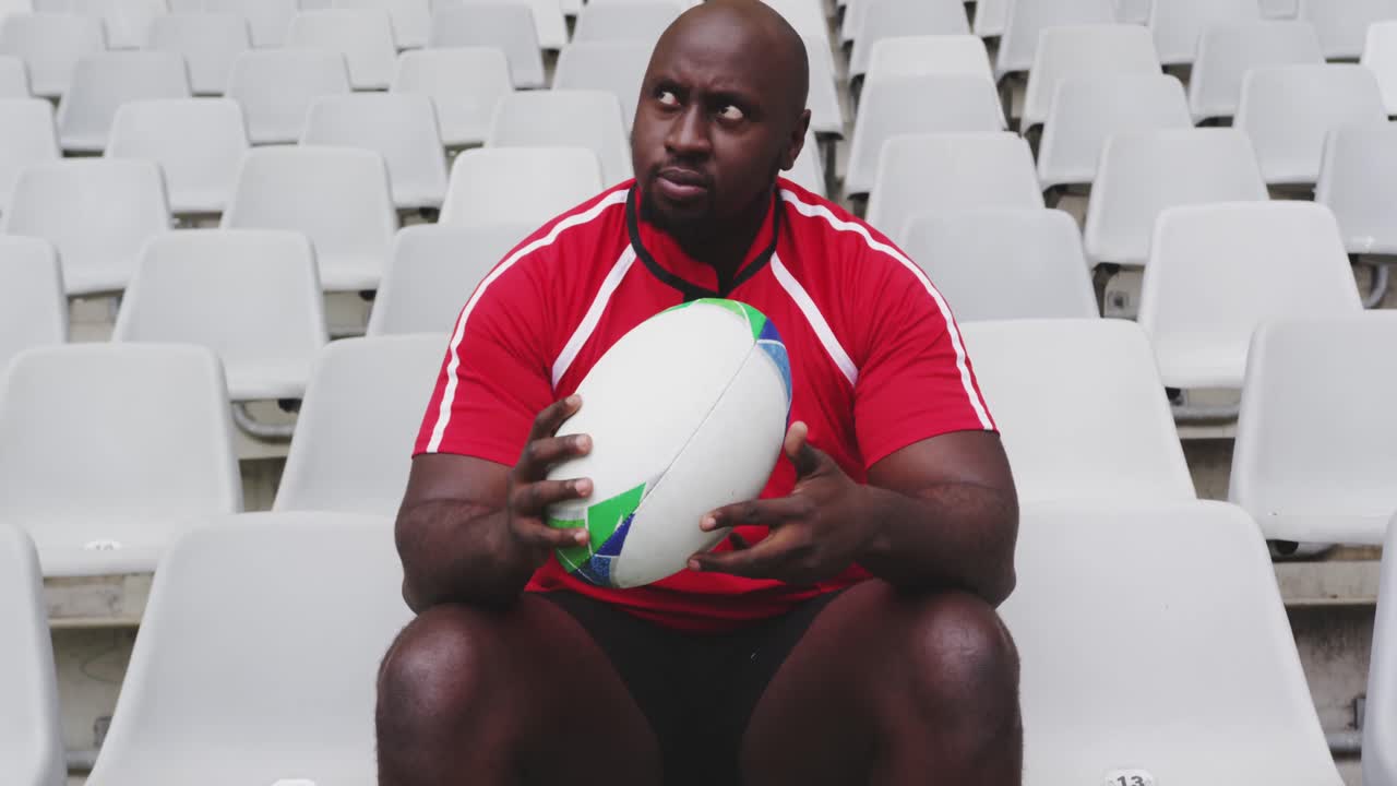 Male rugby player sitting with rugby ball in stadium 4k