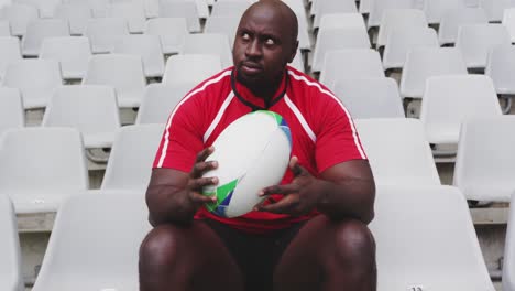 Male-rugby-player-sitting-with-rugby-ball-in-stadium-4k