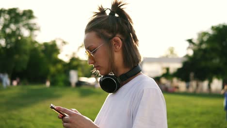 side view of a fancy young girl in white t shirt typing on her mobile phone. black headphones on her neck. spending time in the