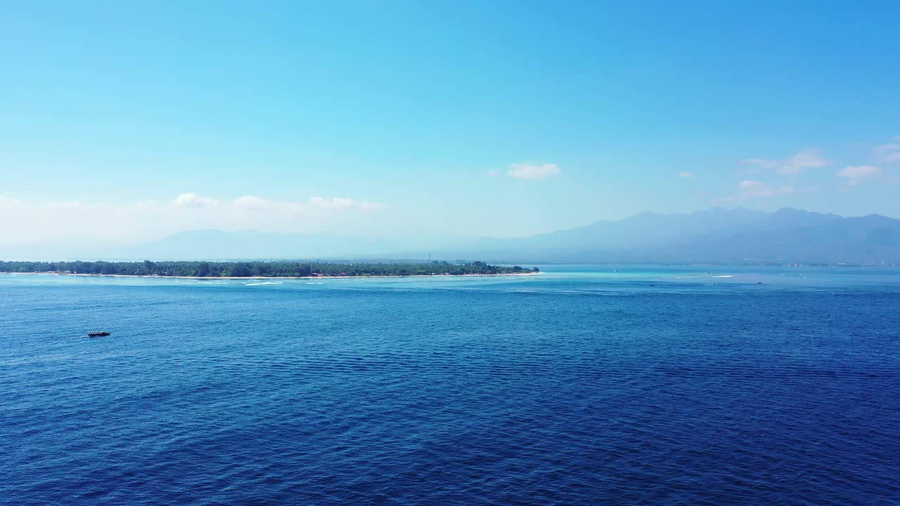Misty morning over low-lying Balinese island surrounded by blue azure sea on a bright sky background, copy space