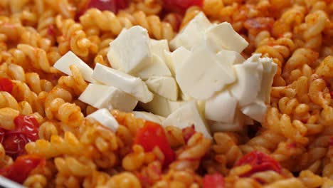 poner media taza de trozos de mozarella en una sartén con pasta fusilli y salsa de tomate, primer plano