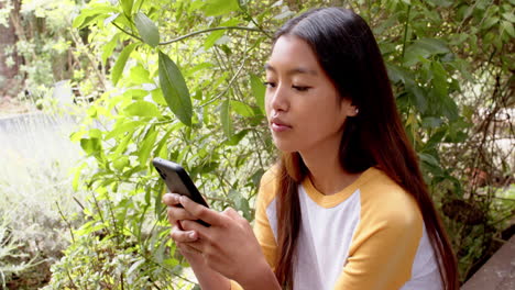 Texting on smartphone, asian young woman smiling in nature, enjoying garden setting, copy space