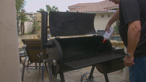 man sprays lighter fluid in to poolside backyard bbq pit to start fire