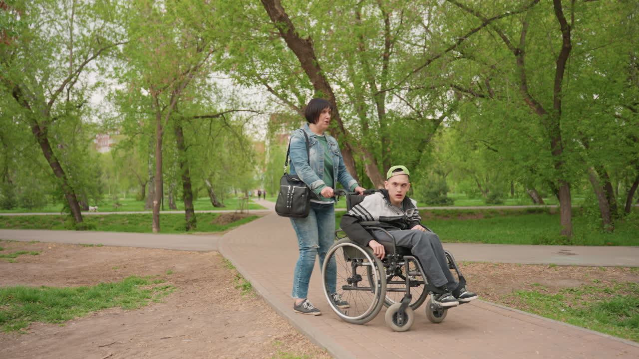 Steady Support During Outdoor Wheelchair Movement, Guide Carefully On Park Pathway With Trees In Sight, Providing Attentive Assistance While Navigating Wheelchair Through Scenic Park Incline