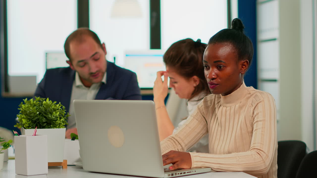alegre mujer de negocios africana escribiendo en la computadora portátil y sonriendo sentada en el escritorio