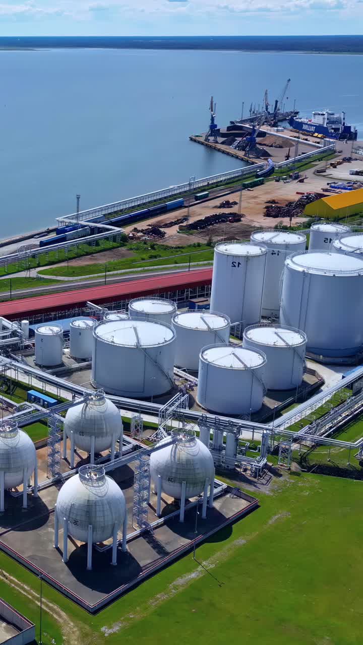 Large white oil storage tanks and pipelines by a coastal port terminal in summer daylight