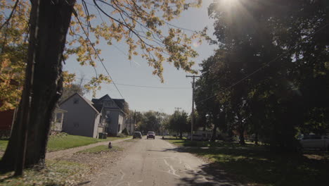 driving a car along a cozy narrow street of a typical american city. the sun shines through the trees