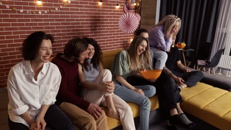 friends watch comedy show on tv and eat popcorn while sitting on a sofa at home