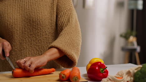 nahaufnahme einer frau zu hause in der küche, die gesundes frisches gemüse für eine vegetarische oder vegane mahlzeit zubereitet und karotten an bord 1 schneidet