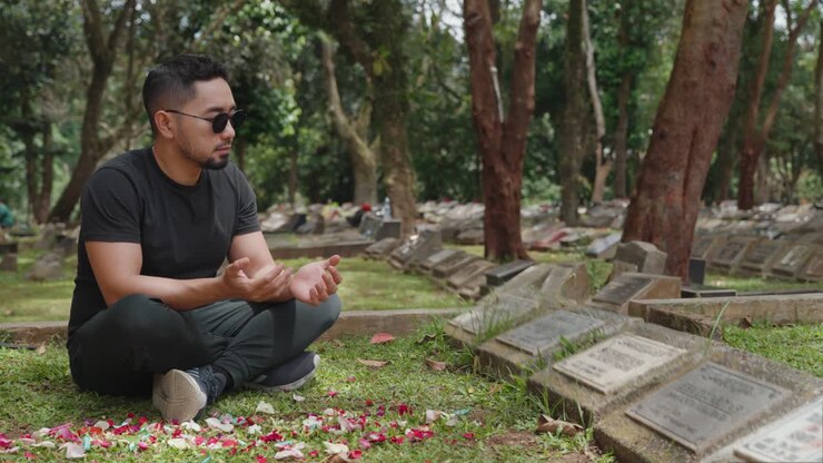 Uomo che prega e tocca una lapide in un cimitero