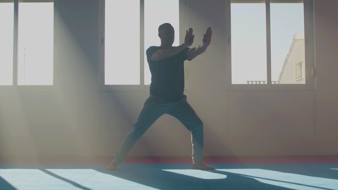 집중된 남자가 빛 속에 타이 치를 연습하고 있습니다.