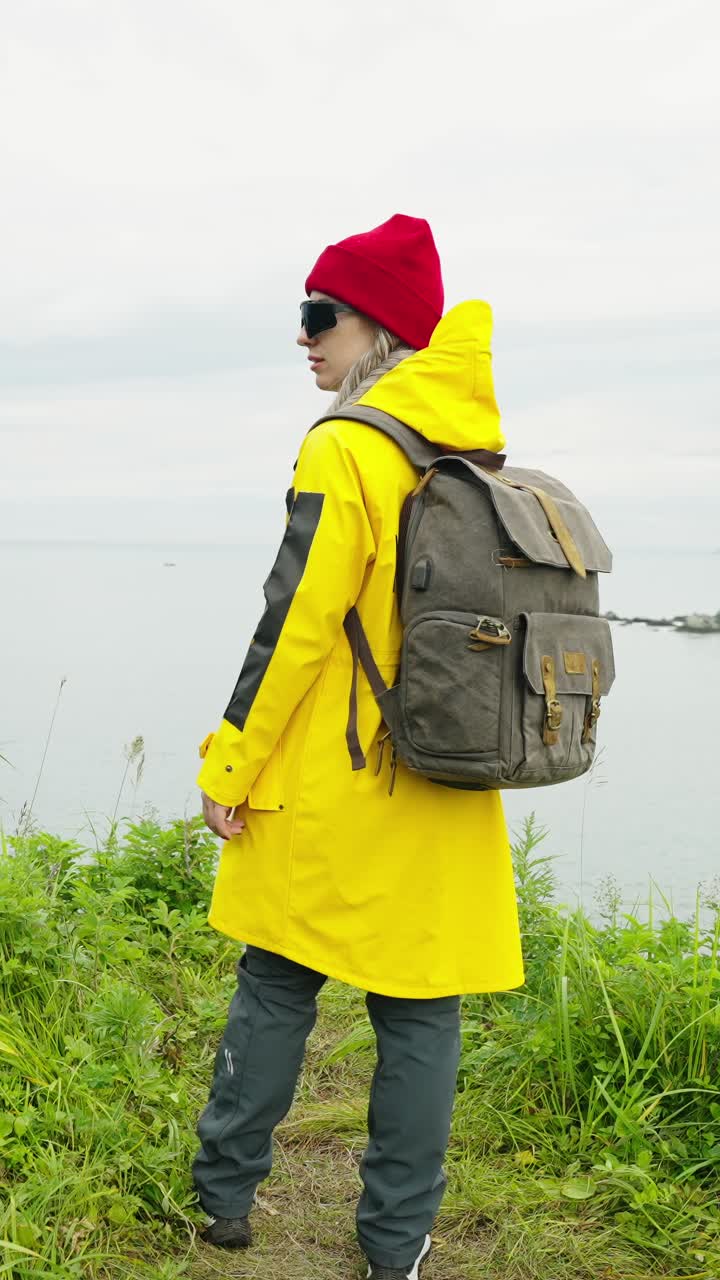 Woman Hiker in Yellow Raincoat Standing on Cliff Overlooking Ocean
