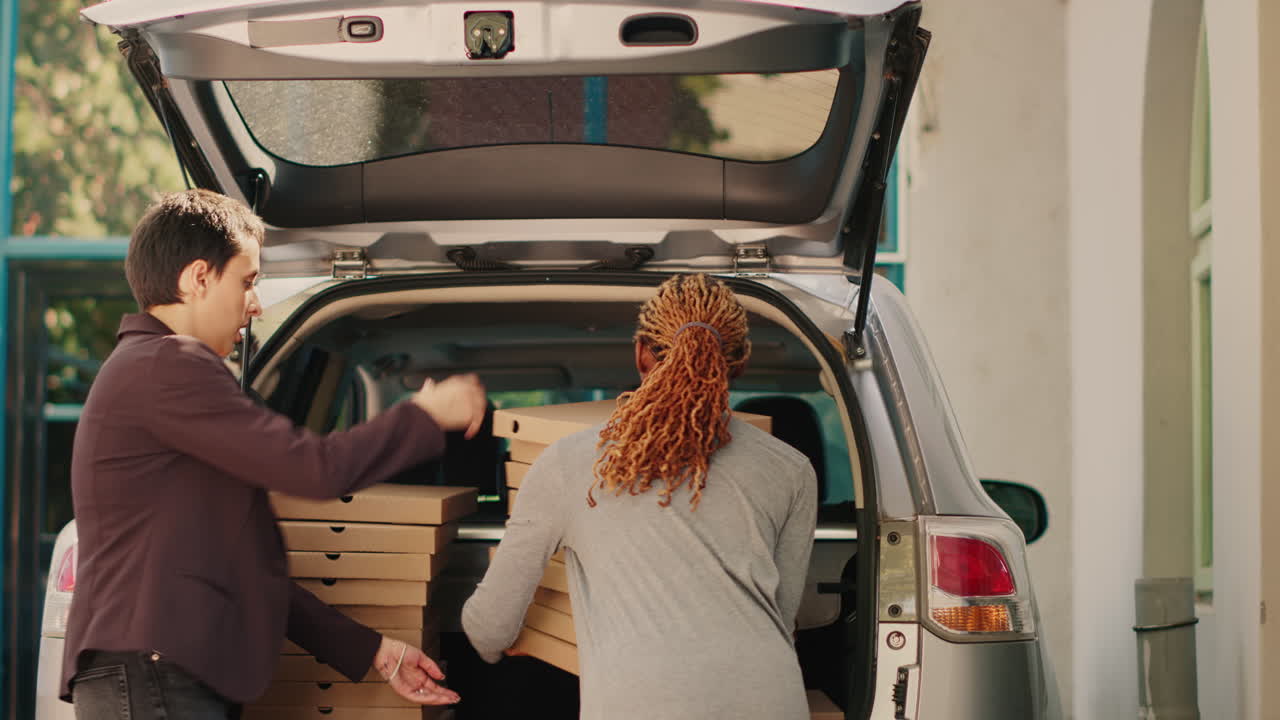 People transferring pizza boxes from a car trunk