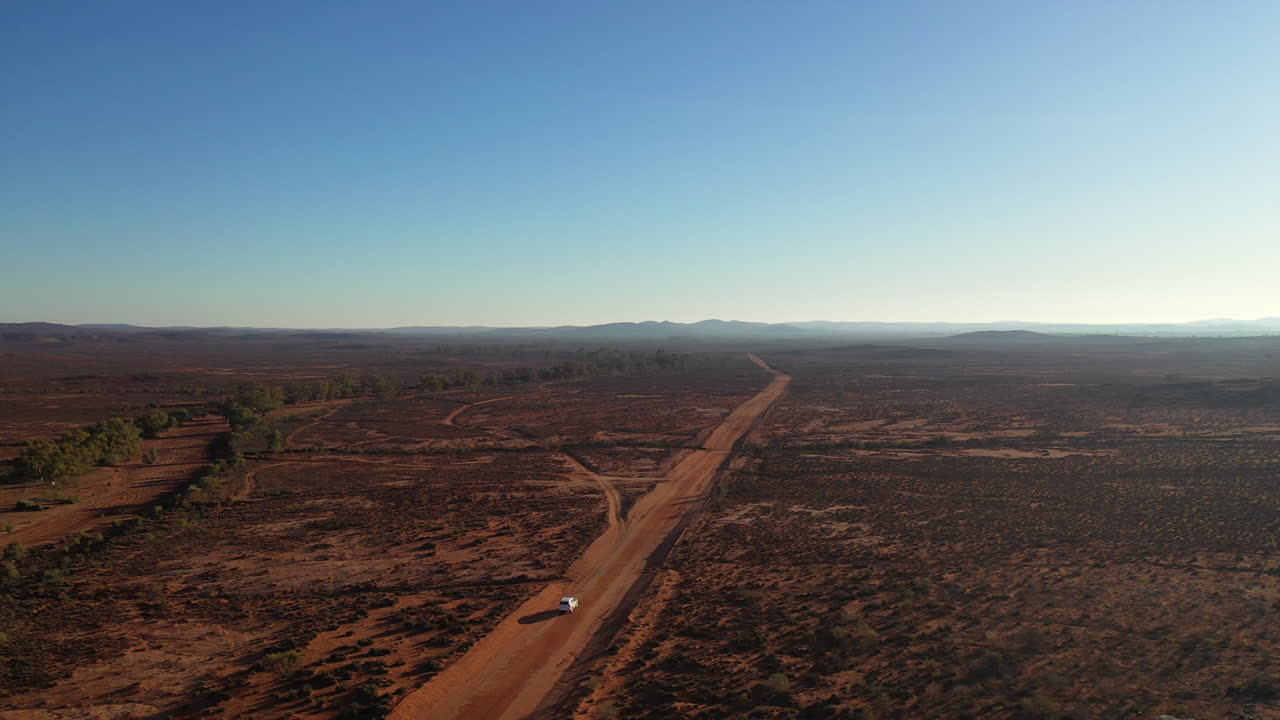 aerial: disparo de avión no tripulado rastreando un vehículo blanco 4wd en su lado derecho mientras conduce a lo largo de una carretera polvorienta del interior lejos de broken hill, australia