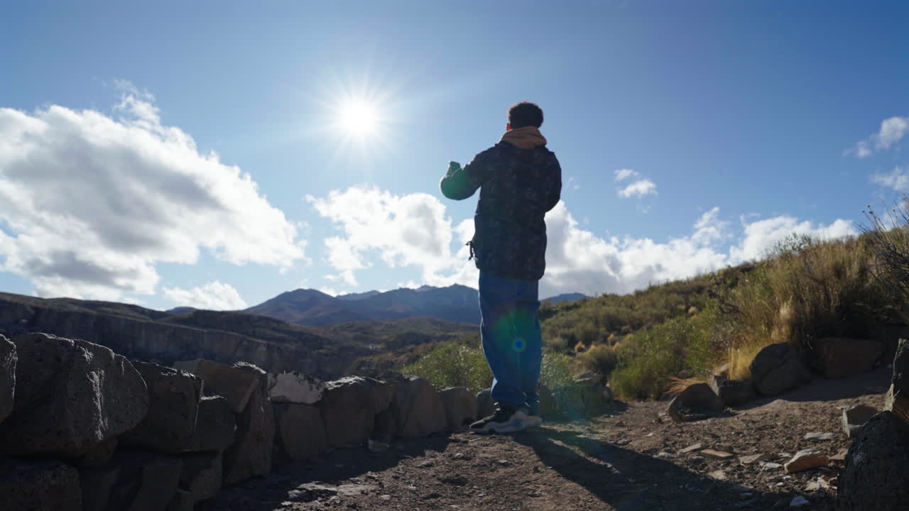 Silhouette of a person raising arm catching to connect a high-frequency cell signal around him on mountain ridge, Malargue, Mendoza, Argentina
