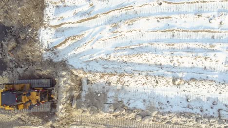 a snowy construction site with heavy machinery and tire tracks, aerial view