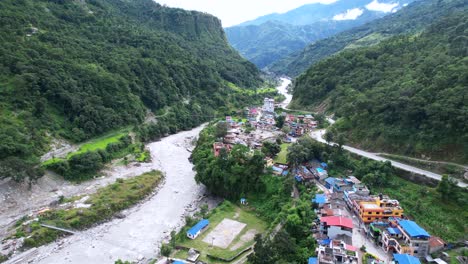 Panoramic-aerial-rural-scene-with-Gandaki-River-and-green-downhill-in-Marpha-Village-in-Nepal,-drone-flying-forward