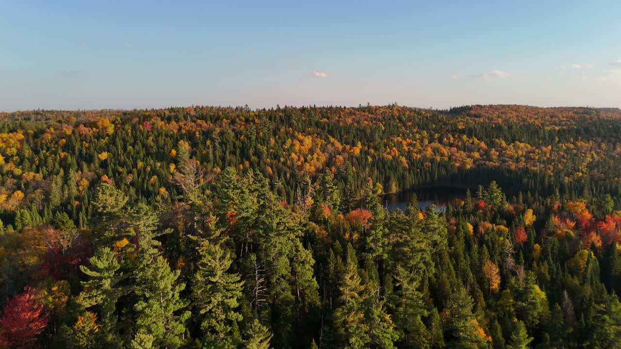 Aerial view of a colorful autumn sunset over a lake and forested mountains in Mauricie, Quebec, Canada. Warm golden light reflects on the calm water
