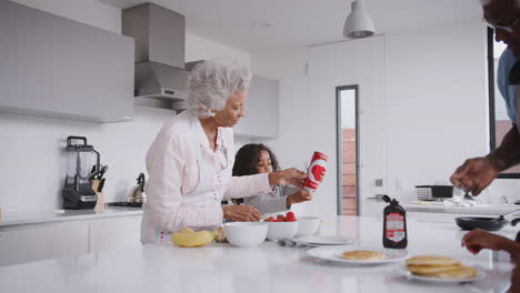 Grandparents-In-Kitchen-With-Grandchildren-Eating-Pancakes-Together