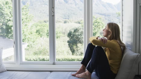 Sad-biracial-woman-sitting-next-to-window-at-home,-slow-motion,-copy-space