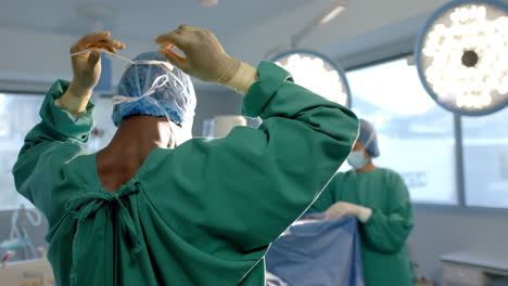 African-american-male-surgeon-tying-face-mask-in-operating-theatre,-copy-space,-slow-motion