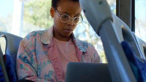 abstract colorful shapes against african american woman using laptop in the bus