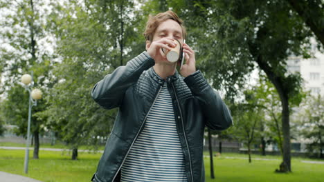 man talking on phone and drinking coffee in park