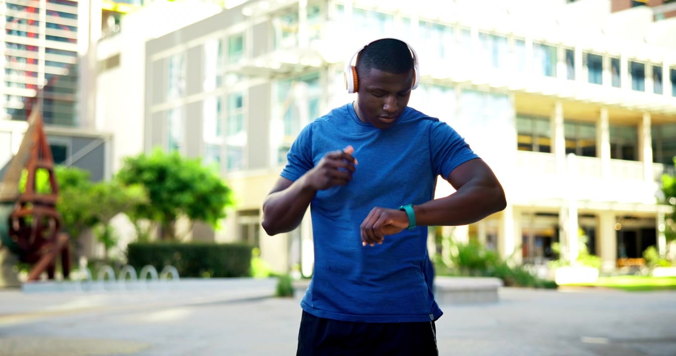 Young Man Putting on Headphones and Checking Smartwatch Outdoors